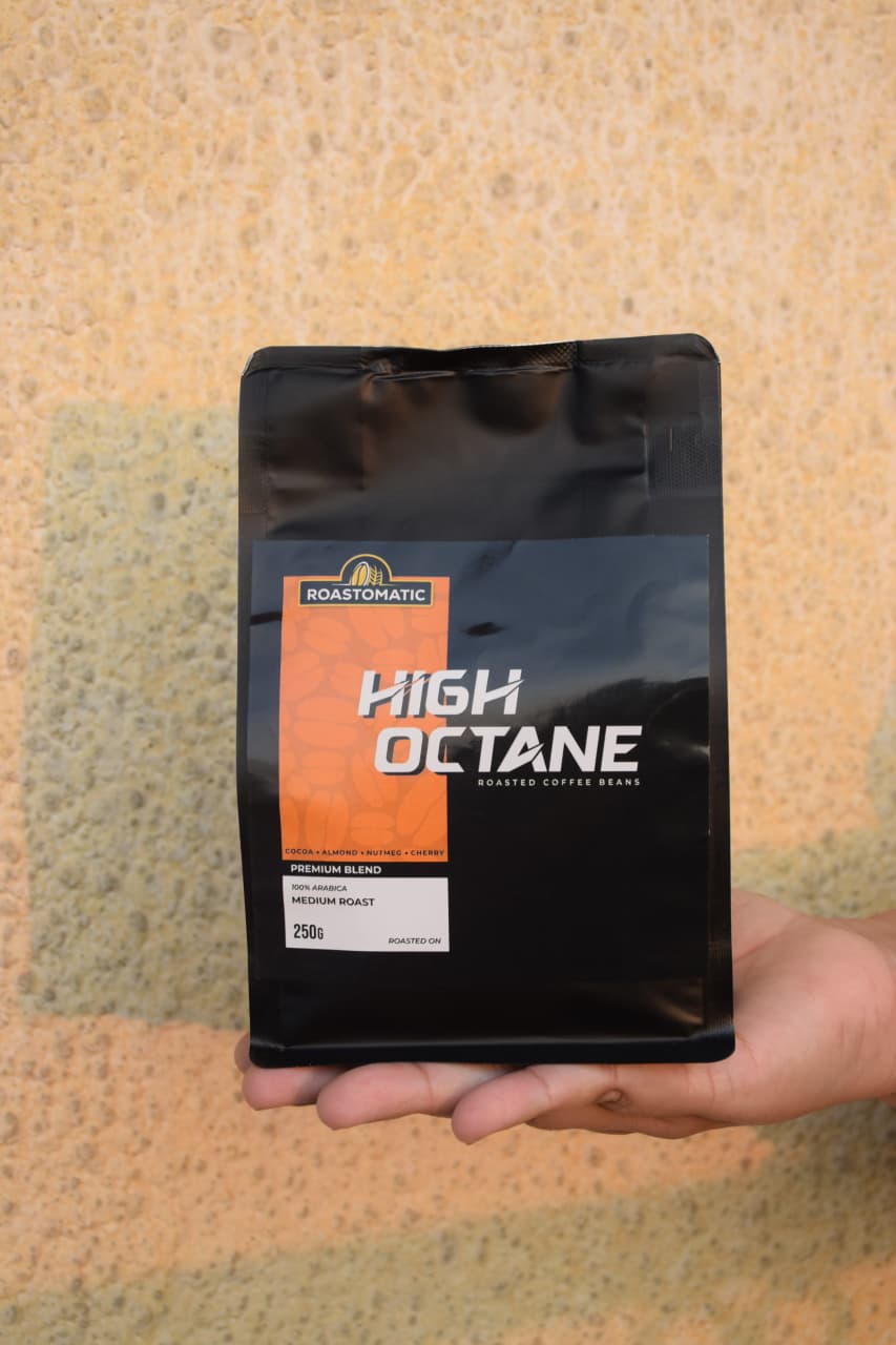 Hand holding a Roastmatic High Octane coffee package against a textured beige background