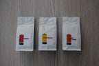 Roastomatic three white coffee bags labeled 'Ethiopia', 'Indonesia', and 'High Octane' on a wooden surface.